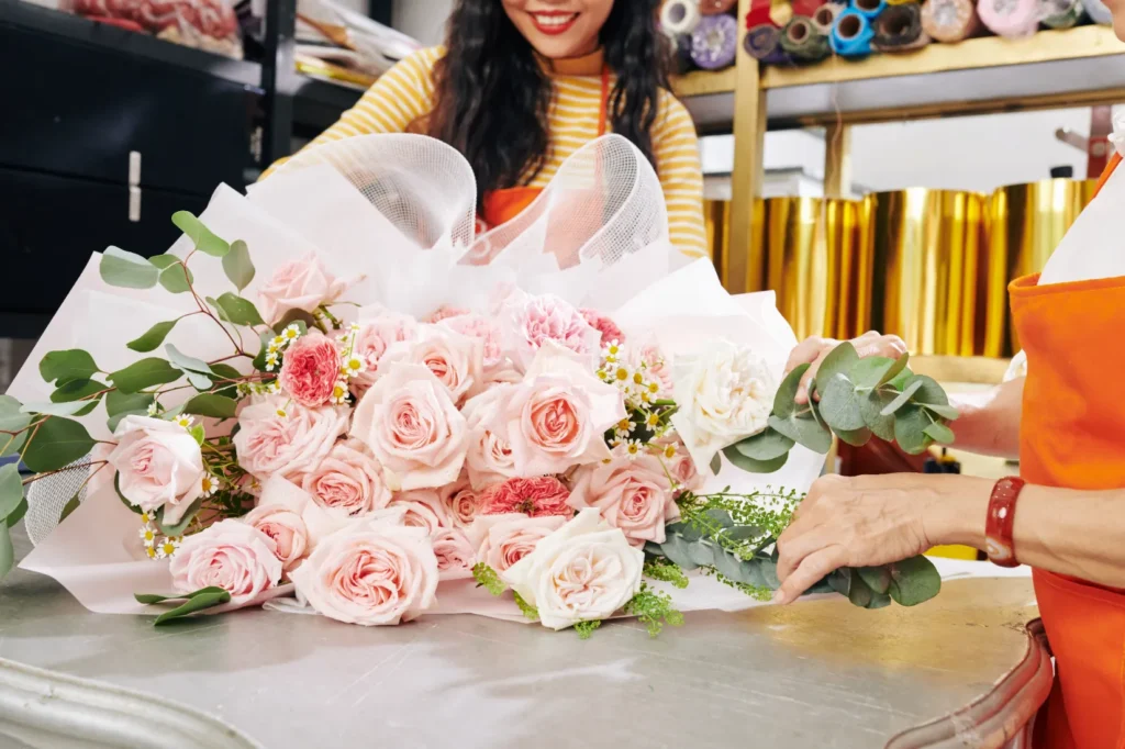 A florist arranging pink roses into a wrapped bouquet for delivery.